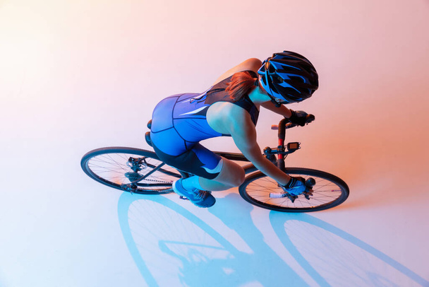 High angle view of female cyclist riding a bicycle isolated against neon background - Photo, image