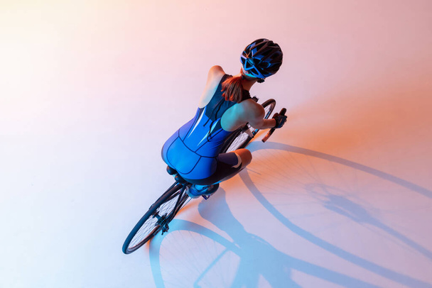 High angle view of female cyclist riding a bicycle isolated against neon background - Фото, изображение