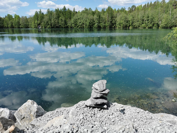 Pyramide de marbre sur la rive du lac Svetloye avec de l'eau turquoise, qui reflète les arbres, et le ciel avec des nuages, dans le parc de montagne Ruskeala. - Photo, image