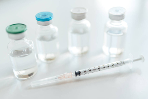 Lahvičky s injekční lahvičkou s vakcínou a injekční stříkačkou na bílém stole. - Fotografie, Obrázek