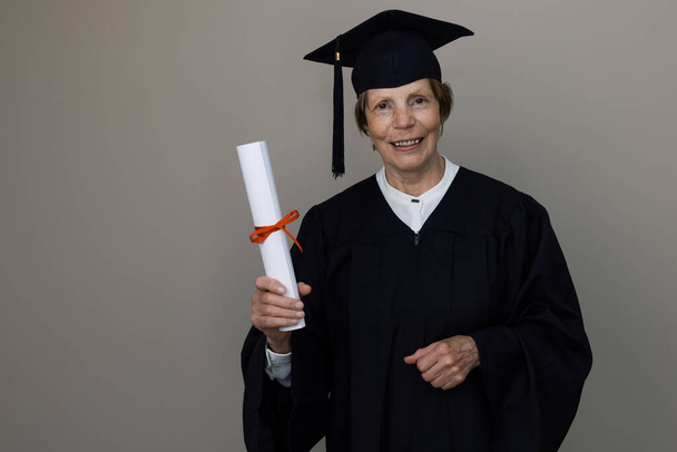 sorridente mulher mais velha graduado em vestido de graduação segurando diploma - Foto, Imagem