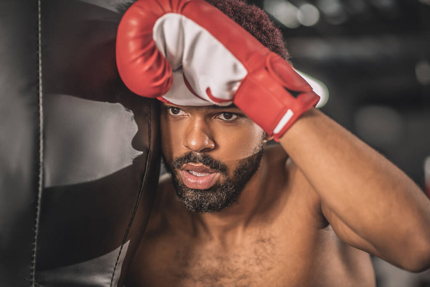 Jeune kickboxer à la peau foncée ayant une séance d'entraînement dans une salle de gym et l'air fatigué - Photo, image