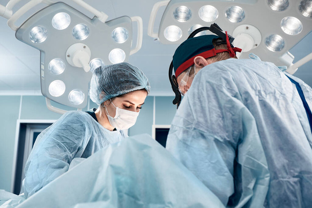 Un equipo de cirujanos masculinos y femeninos en un quirófano moderno, bajo una luz brillante, realizan una operación, medicina moderna. - Foto, Imagen