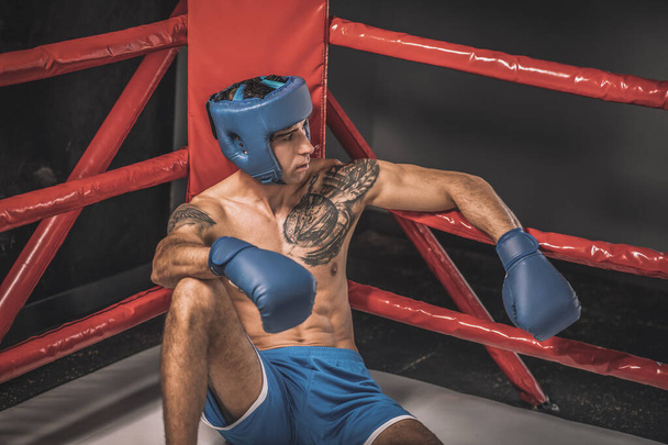 Mladý kickboxer v modré hemlet vypadat unaveně po boji - Fotografie, Obrázek