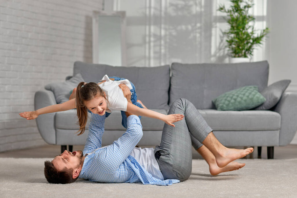 father lying on carpet floor and lifting little child girl - Foto, afbeelding