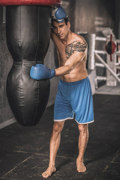 muskularny budować człowiek w niebieski szorty ćwiczenia w siłowni i patrząc wyczerpany - Zdjęcie, obraz