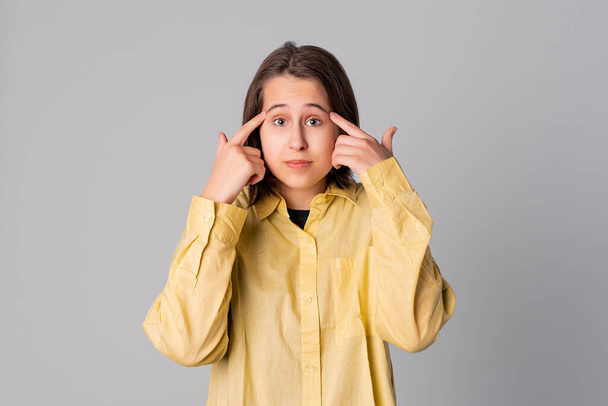 Serious young girl wearing casual yellow shirt pointing to head with two fingers, great idea or thought, good memory. Concept of thinking. Be smart and think - Photo, Image
