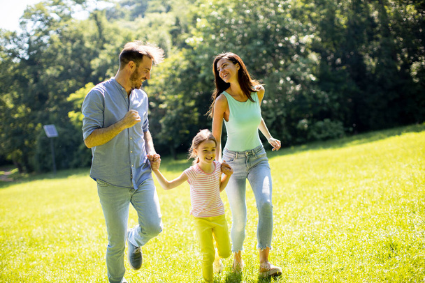 Glückliche junge Familie mit süßer kleiner Tochter läuft an einem sonnigen Tag im Park - Foto, Bild