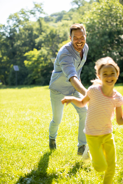 Father chasing his cute little daughter while playing in the park - Photo, Image