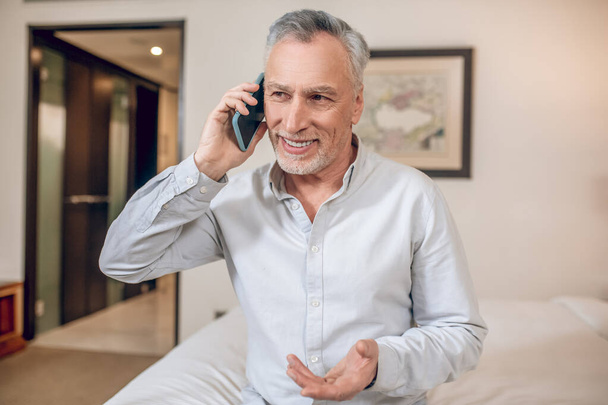 Середнього віку сіро-волохатий бізнесмен розмовляє по телефону і дивиться задіяні
 - Фото, зображення
