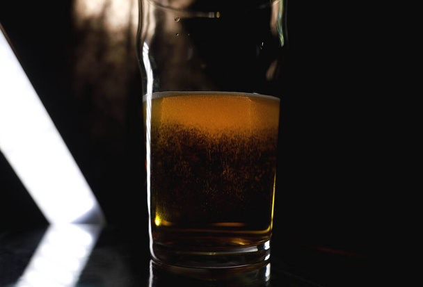 ナイトクラブのバーカウンターでビールのガラスの選択的な焦点。ノニックピントまたはインペリアルピント。アルコール飲料。半空のガラスだ。バーでビールを飲む。アルコール飲料。ナイトクラブライフのコンセプト。アルコール乱用.  - 写真・画像