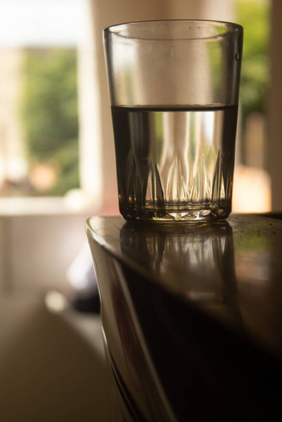 A vertical shot of a half-full glass of water on the table indoors - Fotó, kép