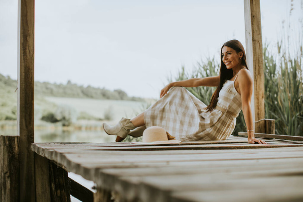穏やかな湖の木の桟橋で若い女性をリラックスさせ - 写真・画像