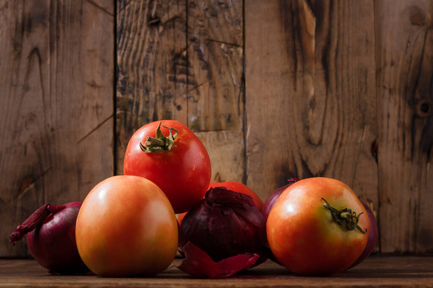Oogsten onrijpe tomaten, rode uien op houten keukentafel. Lokale boer vers biologisch product. Veganistisch milieuvriendelijk geen alternatief voor dierlijk voedsel - Foto, afbeelding