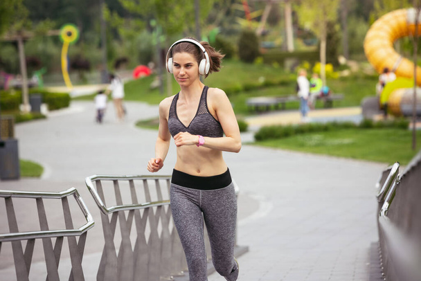 Young female runner, athlete is jogging in the city street in spring sunshine. Beautiful caucasian woman training, listening to music. Concept of sport, healthy lifestyle, movement, activity. - Foto, Imagen