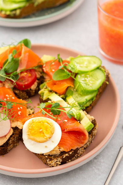 Desayuno sabroso saludable, sándwiches con aguacate y salmón, pepinos y tomates, rábanos y microverduras de guisantes con huevo hervido, batido de pomelo en un vaso - Foto, imagen