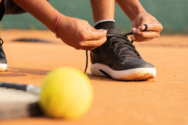 Een close-up shot van een mannelijke atleet strikken zijn schoenen op de tennisbaan - Foto, afbeelding