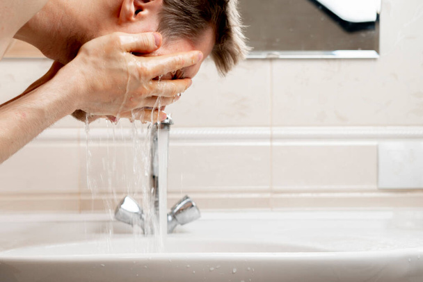 joven barbudo lavándose la cara con salpicaduras en el lavabo en el baño, rutina diaria de la mañana - Foto, Imagen