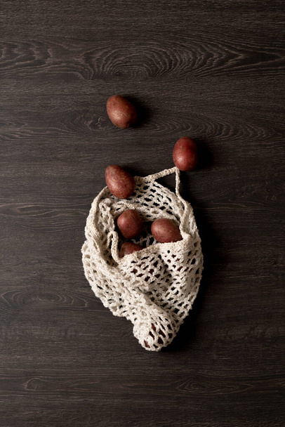 some raw red potatoes in a mesh textile beg flat lay, view from above - Fotó, kép