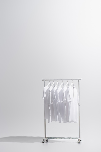 collection of stylish t-shirts hanging on clothes rack isolated on grey  - Zdjęcie, obraz