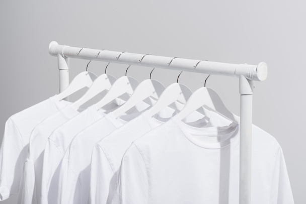 collection of trendy white t-shirts hanging on clothes rack isolated on grey  - Foto, Imagen