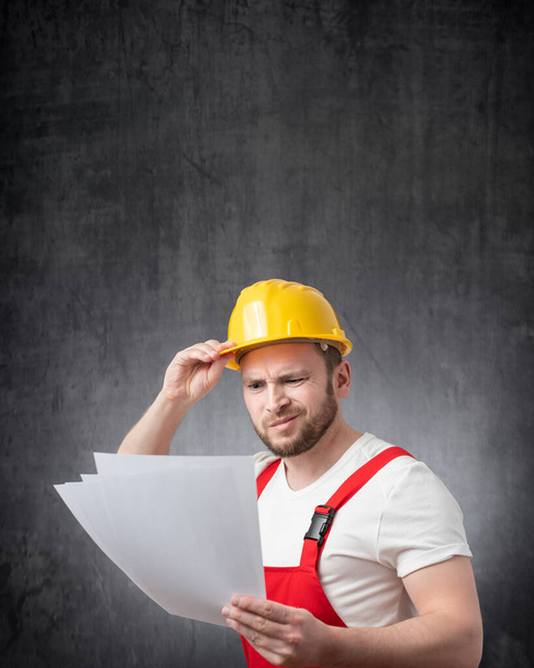A confused construction worker holding papers or documents - Фото, зображення