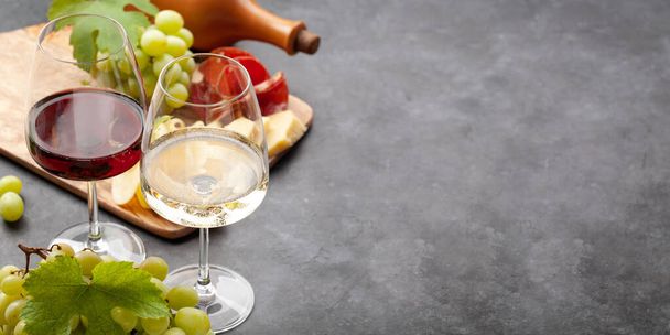 Copas de vino blanco y tinto, tabla de uva y aperitivo con queso y jamón. Con espacio de copia - Foto, Imagen