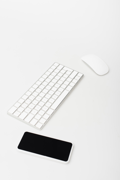 Bilgisayar faresi ve klavye yakınındaki boş ekranlı akıllı telefon beyaz ekranda izole edildi  - Fotoğraf, Görsel