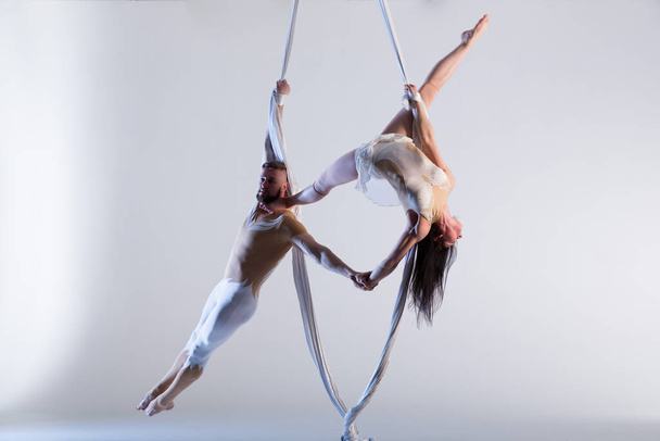 Couple of beautiful aerial gymnasts from Ukraine "Duo lotos" flying on fabric ropes and circle, performing aerial exercise with white fabrics on white background - Фото, зображення