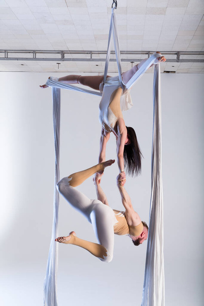 Couple of beautiful aerial gymnasts from Ukraine "Duo lotos" flying on fabric ropes and circle, performing aerial exercise with white fabrics on white background - Photo, Image