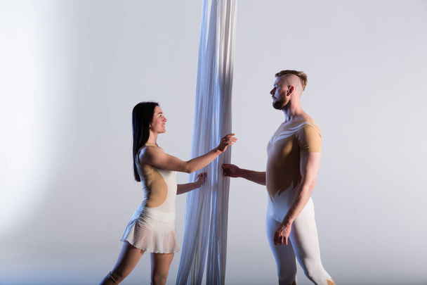 Couple of beautiful aerial gymnasts from Ukraine "Duo lotos" flying on fabric ropes and circle, performing aerial exercise with white fabrics on white background - Foto, immagini