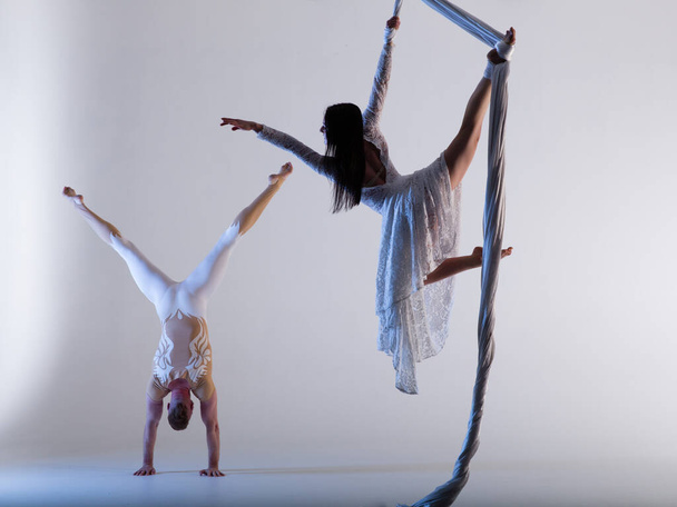 Couple of beautiful aerial gymnasts from Ukraine "Duo lotos" flying on fabric ropes and circle, performing aerial exercise with white fabrics on white background - Fotoğraf, Görsel