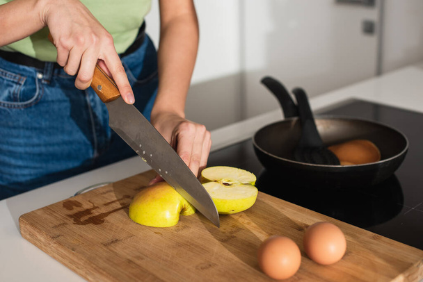 Cropped view of woman cutting apple near eggs on cutting board in kitchen  - Foto, afbeelding