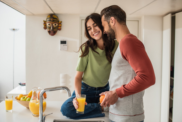 Lächelndes Paar mit Saft und Orange in der Küche  - Foto, Bild