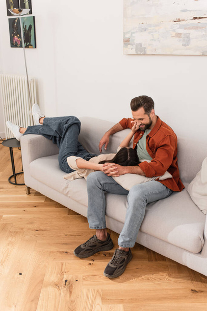 Smiling man holding hand of girlfriend on couch at home  - Photo, Image