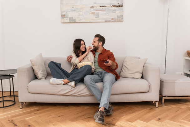 Smiling woman feeding boyfriend with popcorn at home  - Photo, Image