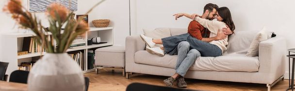 Πλευρική άποψη του νεαρού ζευγαριού αγκαλιάζει στον καναπέ στο σπίτι, πανό  - Φωτογραφία, εικόνα