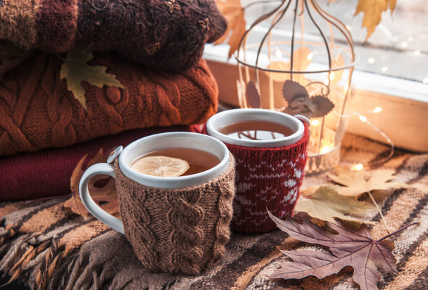 Filiżanka gorącej czarnej herbaty w beżowej dzianinie, drewniana miska z gruszkami, jesienne liście przy oknie - Zdjęcie, obraz