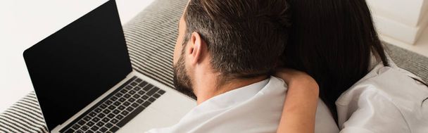 Πίσω όψη του ζευγαριού που βρίσκεται κοντά στο laptop με λευκή οθόνη στο κρεβάτι, banner  - Φωτογραφία, εικόνα