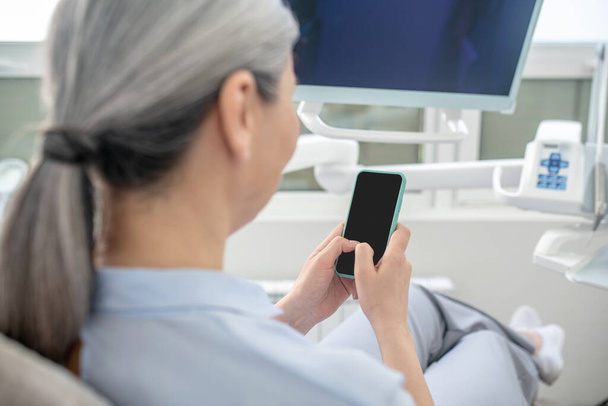 Frau sitzt in Zahnarztpraxis und textet auf ihrem Smartphone - Foto, Bild