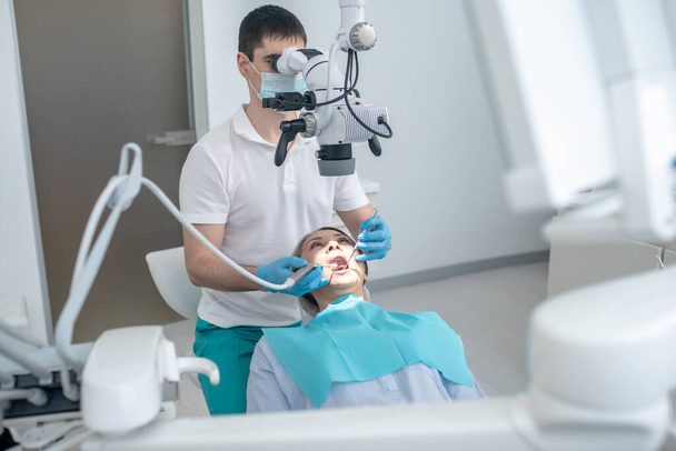 Chirurgien dentaire masculin travaillant avec le patient et utilisant un instrument médical optique - Photo, image