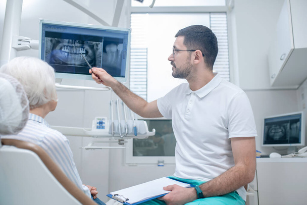 Male young dentist explaining the results of xray to his female patient - Foto, immagini