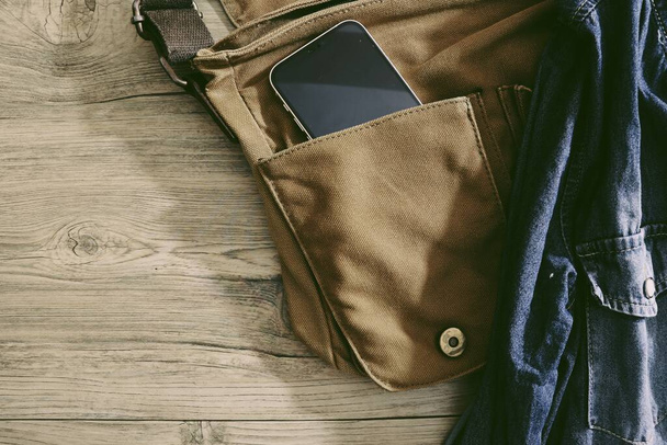 Smart τηλέφωνο και σακάκι τζιν με καφέ τσάντα σε ξύλινο τραπέζι φόντο - Φωτογραφία, εικόνα
