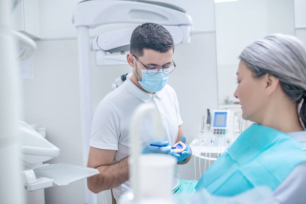 Młody dentysta pokazuje protezę swojej pacjentce - Zdjęcie, obraz