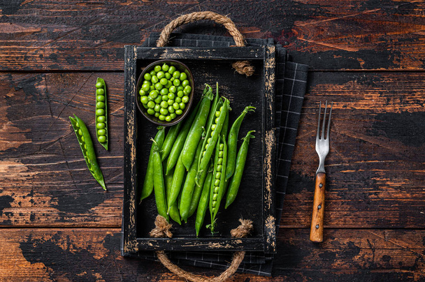 Raw green pea pods in a wooden tray. Dark wooden background. Top view - Photo, Image
