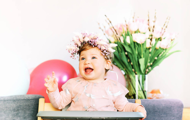 Spring portrait of adorable baby sitting in a chair, wearing flower headband - Foto, imagen