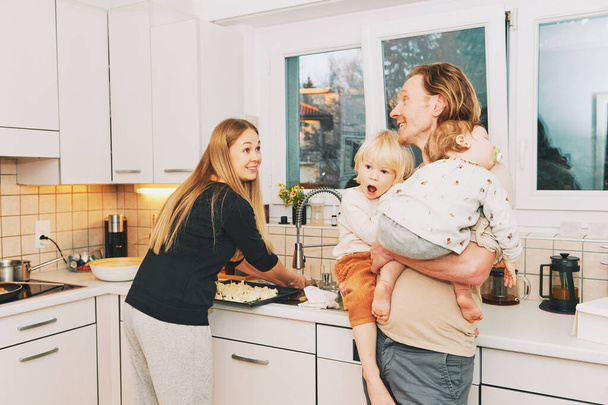 Vida familiar, madre cocinando la cena, padre sosteniendo bebé dormido y niño emocionado, paternidad feliz - Foto, Imagen
