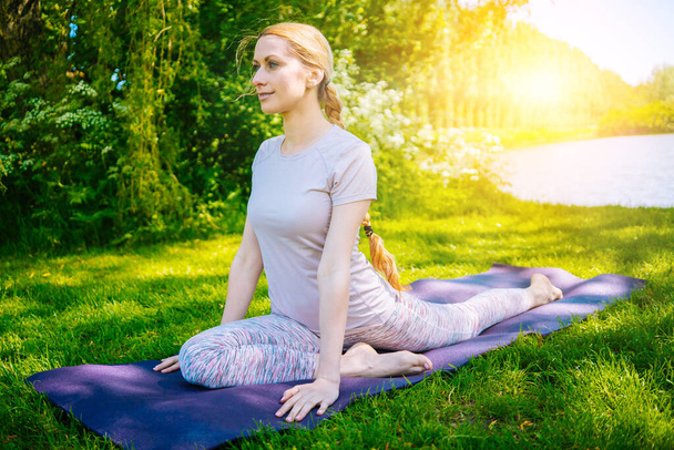 Młoda kobieta uprawiająca jogę w parku. Dziewczyna rozciąga ćwiczenia w pozycji do jogi. szczęśliwa i zdrowa kobieta siedząca w pozycji lotosu i ćwicząca jogę. medytacja i sport na zachodzie słońca na zewnątrz. - Zdjęcie, obraz