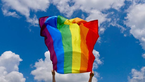 Человек, держащий флаг ЛГБТ на фоне неба - Фото, изображение