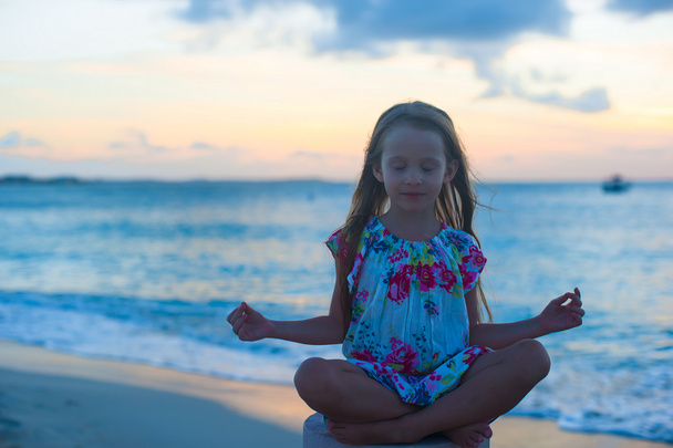 Красивая маленькая девочка сидит в позе лотоса на экзотическом пляже
 - Фото, изображение